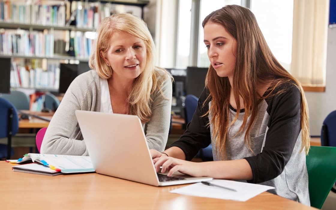 Coach and student planning coursework together on a laptop in a library