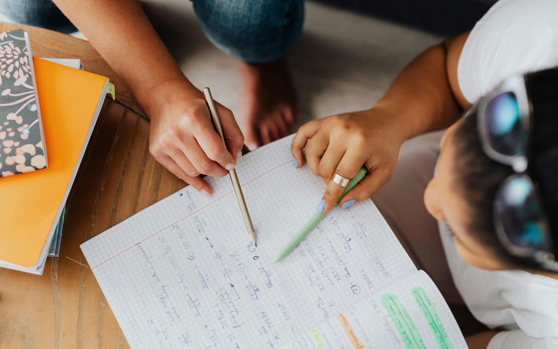 Tutor and student working through math problems in a graph-paper notebook