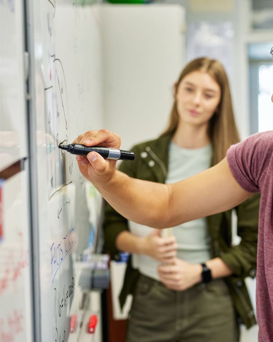 Student solving a problem on the whiteboard while classmates look on