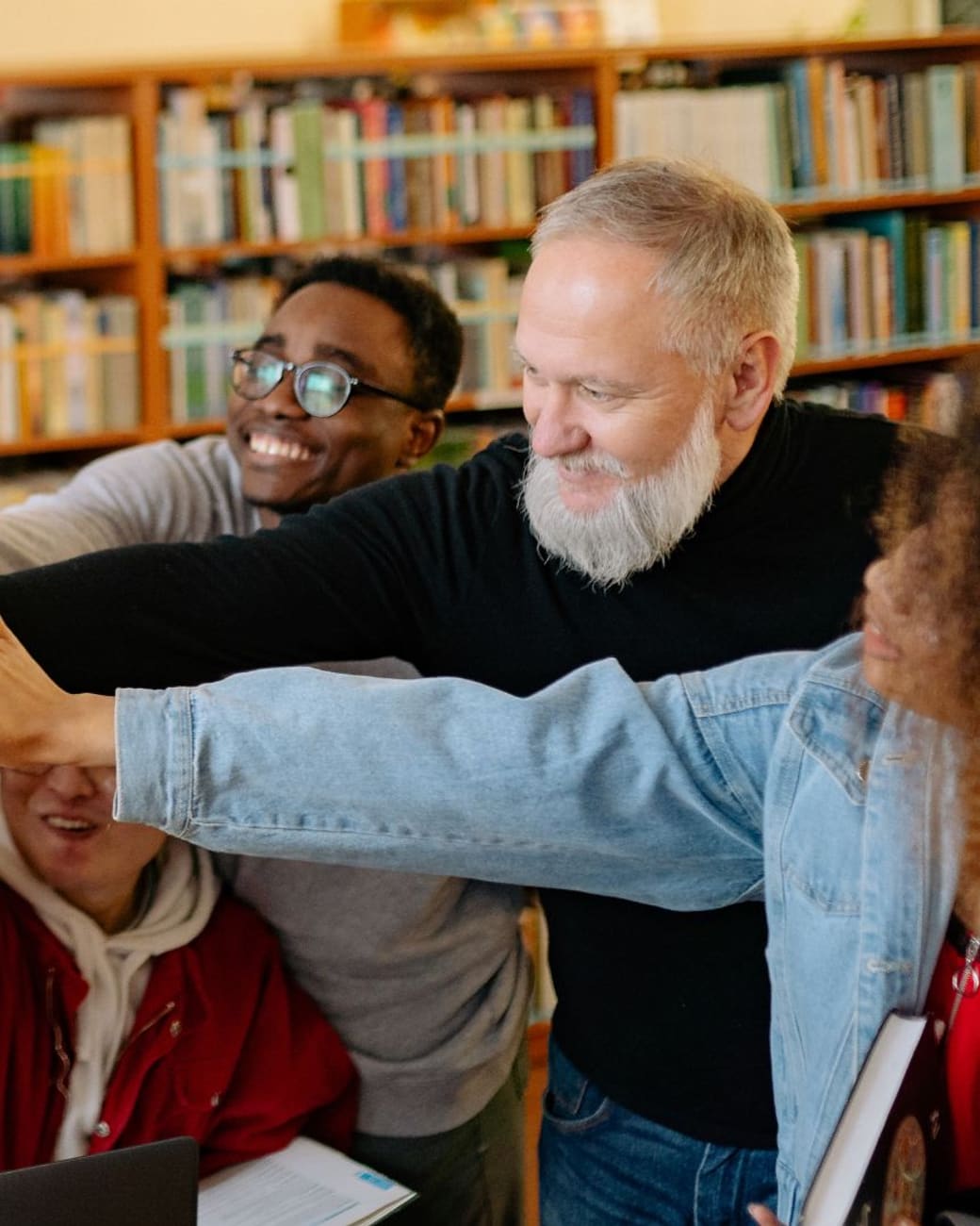Students and mentor celebrating a milestone with a group high-five in the library